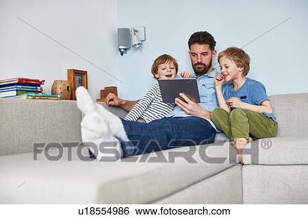Stock Photograph - Father and sons on sofa using digital tablet. Fotosearch