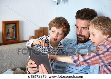 Father and sons on sofa using digital tablet View Large Photo Image Stock Photograph - Father and sons on sofa using digital tablet. Fotosearch