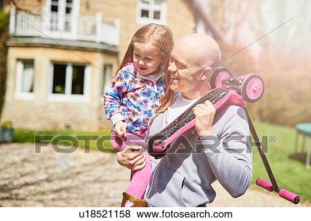 Stock Photo - Father carrying daughter and scooter. Fotosearch