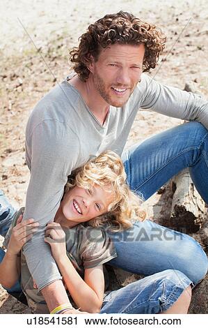 Stock Image - Father sitting with arm around smiling son looking at camera. Fotosearch