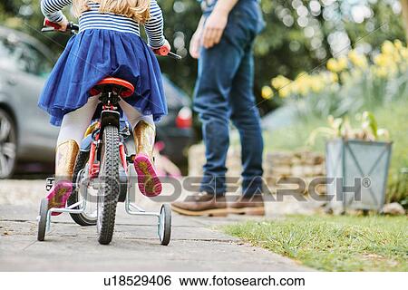 Father teaching daughter to ride bicycle on street View Large Photo Image Stock Photograph - Father teaching daughter to ride bicycle on street. Fotosearch