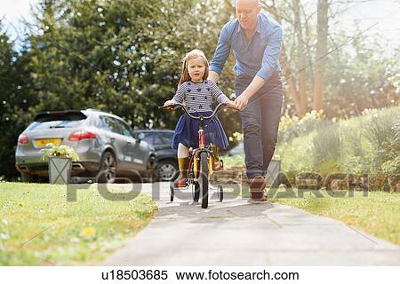Father teaching daughter to ride bicycle on street View Large Photo Image Stock Photography - Father teaching daughter to ride bicycle on street. Fotosearch
