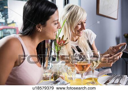 Stock Photo - Friends using smartphone during lunch in restaurant. Fotosearch