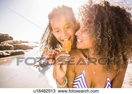 Stock Image - Girl and mother sharing ice lolly on beach, Cape Town, South Africa. Fotosearch