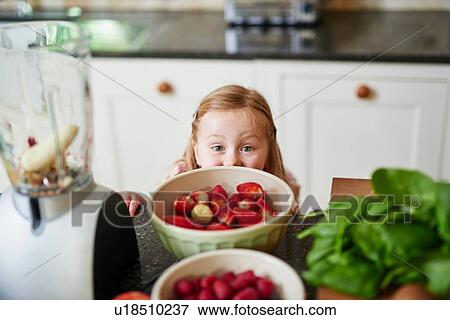 Stock Photo - Girl peeking over bowls of strawberries of kitchen counter. Fotosearch