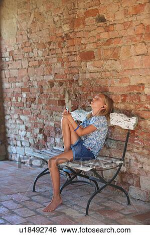 Girl sitting on bench listening to earphone music, Buonconvento, Tuscany, Italy View Large Photo Image Stock Photograph - Girl sitting on bench listening to earphone music, Buonconvento, Tuscany, Italy. Fotosearch
