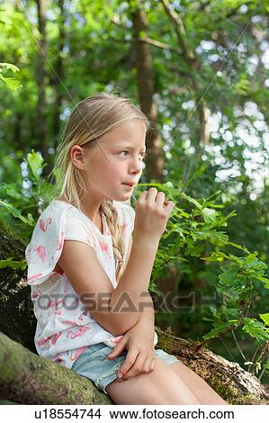 Girl sitting on branch chewing grass View Large Photo Image Picture - Girl sitting on branch chewing grass. Fotosearch