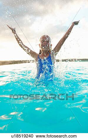Stock Image - Girl splashing in swimming pool, Buonconvento, Tuscany, Italy. Fotosearch