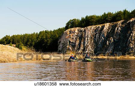 Stock Photo - Group of friends on river in dinghies by rock face. Fotosearch