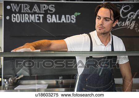 Stock Photography - Happy restaurateur wiping service counter. Fotosearch