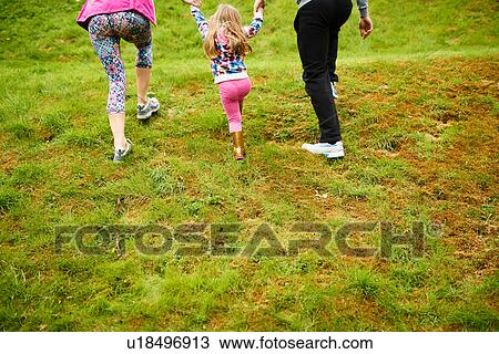 Stock Image - Low section rear view of parents holding girls hands. Fotosearch