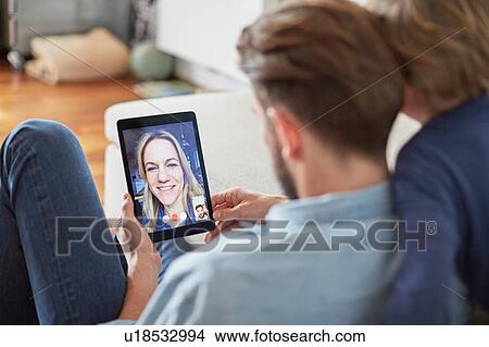 Picture - Man and son sitting on floor talking to mother on digital tablet video call. Fotosearch