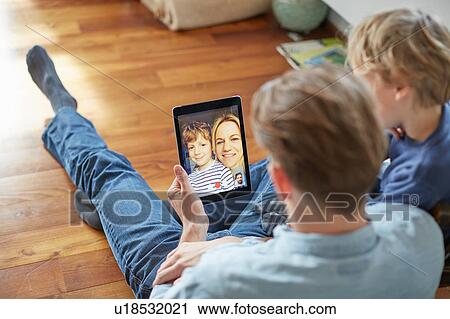 Man and son sitting on floor talking to mother and brother on digital tablet video call View Large Photo Image Stock Image - Man and son sitting on floor talking to mother and brother on digital tablet video call. Fotosearch