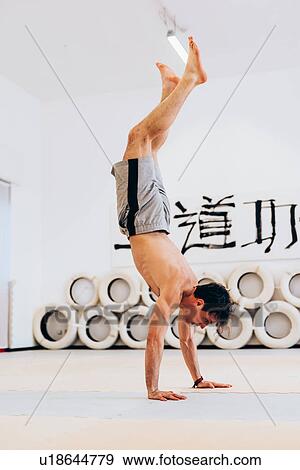 Stock Photo - Man doing handstand holding plastic bottle in feet. Fotosearch