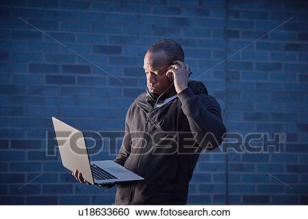 Man holding laptop listening on headphones View Large Photo Image Stock Image - Man holding laptop listening on headphones. Fotosearch