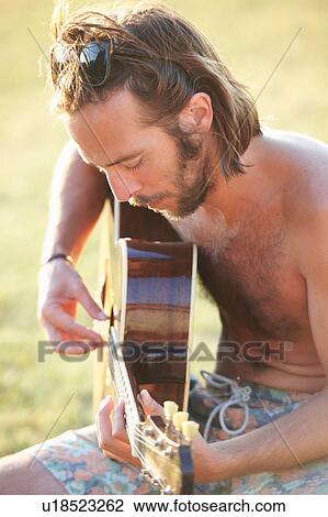 Stock Image - Man in garden playing acoustic guitar, Buonconvento, Tuscany, Italy. Fotosearch