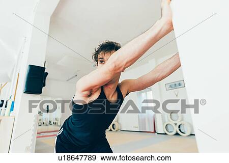 Stock Photo - Man in gym leaning against wall stretching. Fotosearch