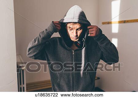 Stock Image - Man in shade wearing hooded top looking down. Fotosearch