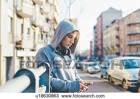 Man in urban area wearing hooded top and headphones looking down at smartphone View Large Photo Image Stock Image - Man in urban area wearing hooded top and headphones looking down at smartphone. Fotosearch
