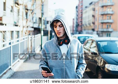 Man in urban area wearing hooded top and headphones looking down at smartphone View Large Photo Image Stock Image - Man in urban area wearing hooded top and headphones looking down at smartphone. Fotosearch