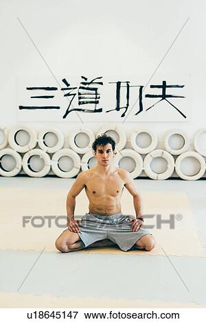 Stock Photo - Man kneeling on exercise mat looking at camera. Fotosearch