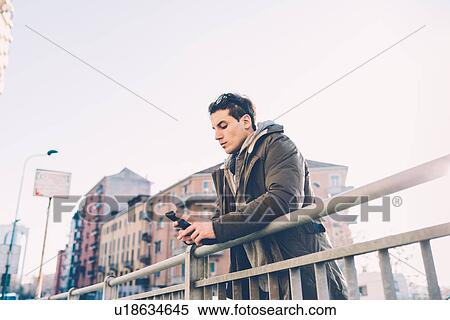 Man leaning against railings using smartphone View Large Photo Image Stock Photography - Man leaning against railings using smartphone. Fotosearch