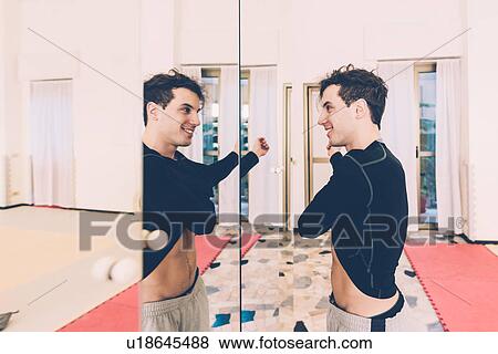 Stock Photo - Man looking in mirror taking off t-shirt smiling. Fotosearch