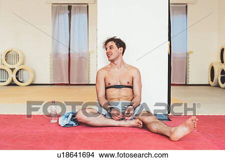Picture - Man sitting leaning against column wearing heart rate monitor on chest. Fotosearch