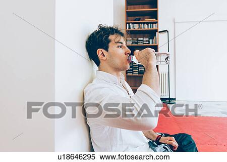 Stock Photography - Man sitting leaning against column drinking water from bottle. Fotosearch