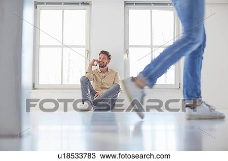 Stock Image - Man sitting on floor talking on smartphone in new home. Fotosearch