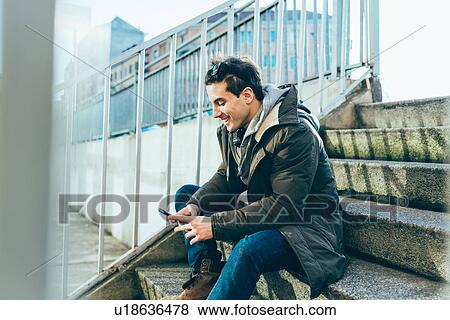 Stock Photo - Man sitting on step using smartphone smiling. Fotosearch