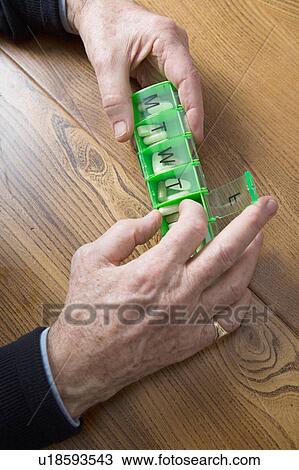 Stock Image - Man taking medication out of pill box. Fotosearch