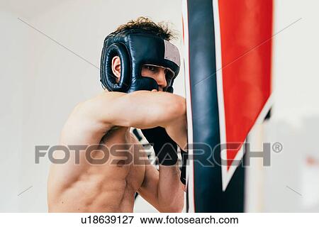Stock Photo - Man wearing head protector sparring with punchbag. Fotosearch