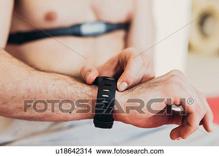 Picture - Man wearing heart rate monitor on chest checking wrist watch. Fotosearch