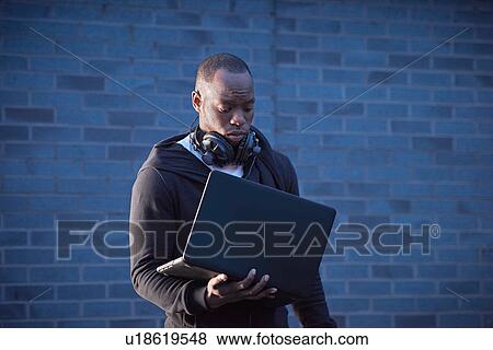 Stock Photo - Man with headphones holding laptop. Fotosearch