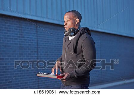 Stock Image - Man with headphones using handheld keyboard. Fotosearch