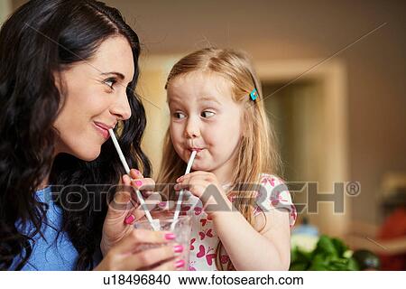 Stock Image - Mother and daughter face to face drinking smoothie with straws. Fotosearch