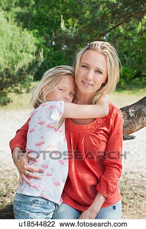 Stock Image - Mother and daughter leaning against tree looking at camera smiling. Fotosearch