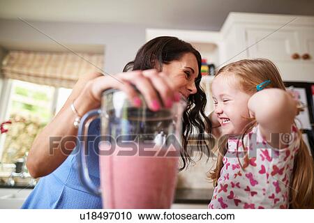 Stock Image - Mother and daughter making smoothies in noisy blender. Fotosearch