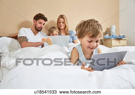 Mother and father in bed with sons using technology View Large Photo Image Stock Image - Mother and father in bed with sons using technology. Fotosearch