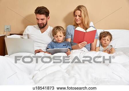 Mother and father in bed with sons using technology and reading book View Large Photo Image Stock Image - Mother and father in bed with sons using technology and reading book. Fotosearch