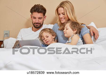 Mother and father in bed with sons looking at digital tablet View Large Photo Image Stock Photo - Mother and father in bed with sons looking at digital tablet. Fotosearch