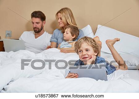 Mother and father in bed with sons using technology View Large Photo Image Stock Photo - Mother and father in bed with sons using technology. Fotosearch