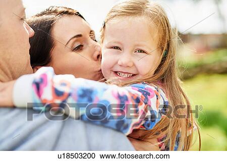 Stock Image - Over shoulder view of mother kissing smiling daughter on cheek. Fotosearch