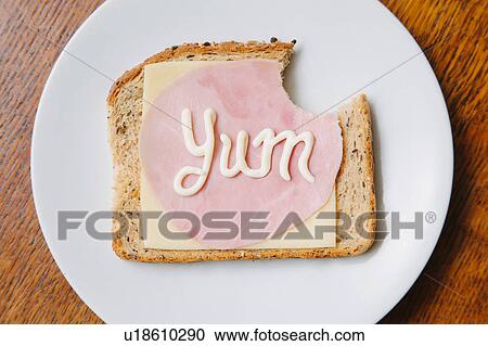 Stock Image - Overhead view of the word yum written on ham and cheese on bread in mayonnaise. Fotosearch