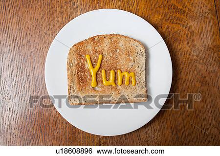 Stock Photograph - Overhead view of the word yum written on ham on toast in mustard. Fotosearch