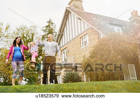 Stock Photo - Parents swinging daughter in garden. Fotosearch