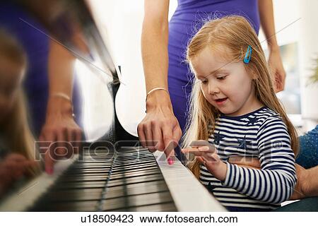 Stock Image - Parents teaching daughter to play piano. Fotosearch
