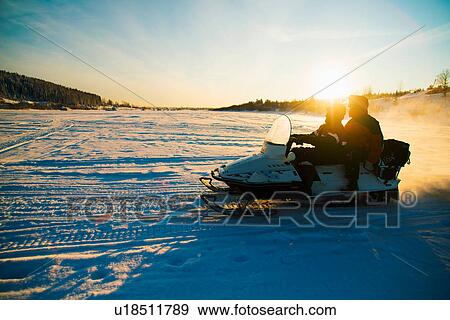 Stock Photo - People on snowmobile on snow covered landscape. Fotosearch