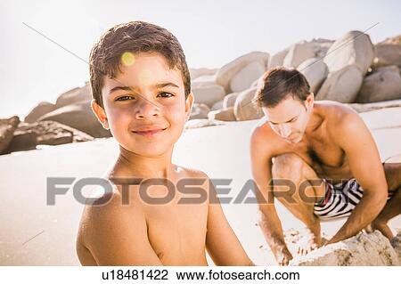 Stock Image - Portrait of boy and father making sandcastle on beach, Cape Town, South Africa. Fotosearch
